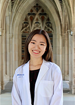 Student Jamie Lim wearing white coat smiling at camera under archways