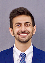 Headshot of student smiling at camera with dark brown hair wearing blue suit and blue checkered tie