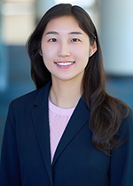 Student smiling at camera with dark straight hair falling in front of left shoulder, wearing blue blazer over light pink shirt