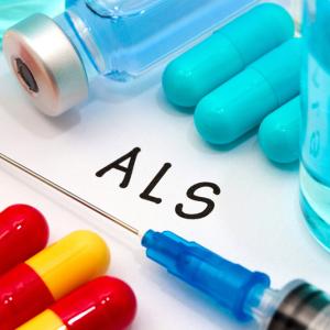 The letters ALS written on a piece of paper, surrounded by pills, a syringe and vials of medicine